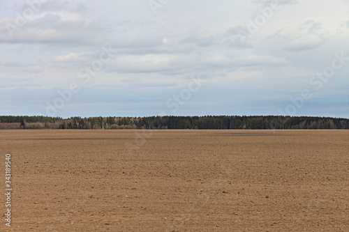 Beautiful vast brown ploughed field landscape against a blue sky on a spring day — land cultivation farm, agriculture, rural life