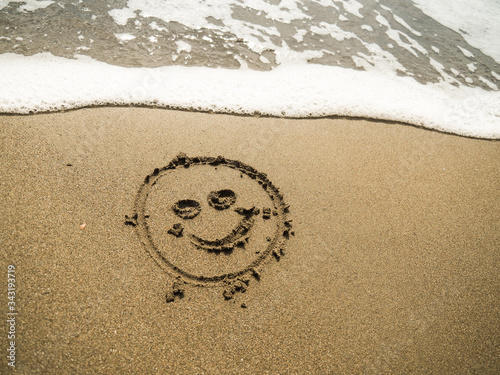 smiley written in beach sand with blue ocean water foam in the background  photo