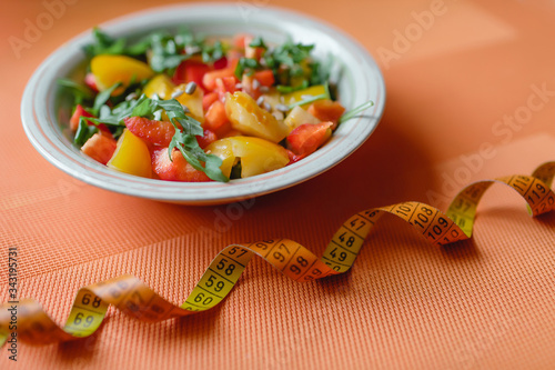 Measuring tape and salad on orange background