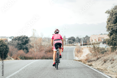 Fototapeta Naklejka Na Ścianę i Meble -  Back view of female cyclist cycling to the village