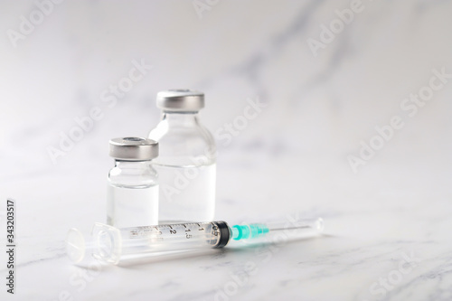 Syringe and vaccine with white marble background.