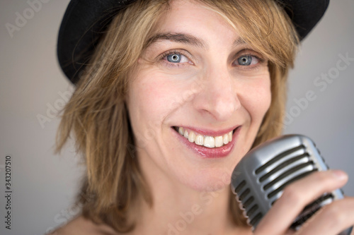 Portrait of cheerful blonde woman singing a song with a vintage silver microphone. Woman holding a vintage microphone and performing live music. Music equipment and musical career concept.