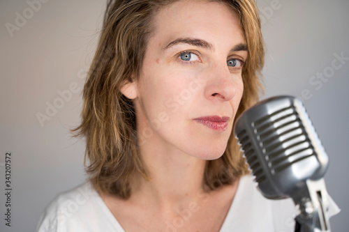 Portrait of serious caucasian woman singing a song with a vintage silver microphone. Woman holding a vintage microphone and performing live music. Music equipment and musical career concept.