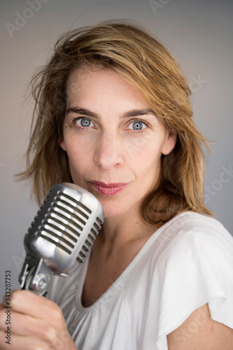 Beautiful caucasian woman holding a vintage microphone. Music and live performing concept. Singer woman singing on a professional recording music studio. Arts, entertainment and musical lifestyle.