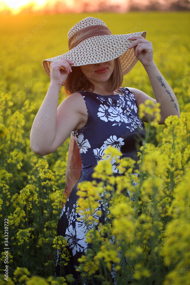 Beautiful girl in a straw hat walks in a field at sunset