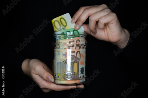 Woman holding a jar full of money. Woman pulling money out of the jar.