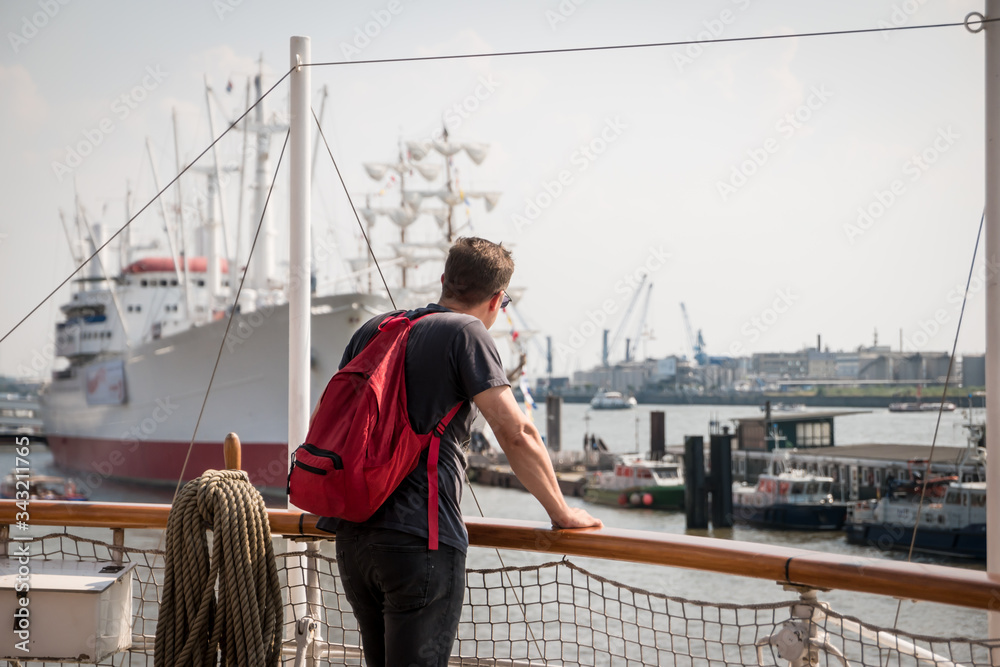 A tourist stands on a ship deck overlooking the harbour and other boats in the port A tourist stands on a ship deck overlooking the harbour and other boats in the port