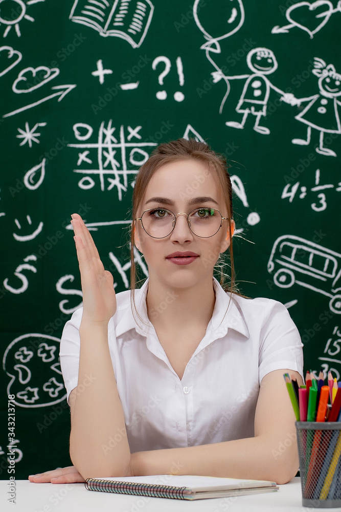 Young teacher is sitting near blackboard in classroom