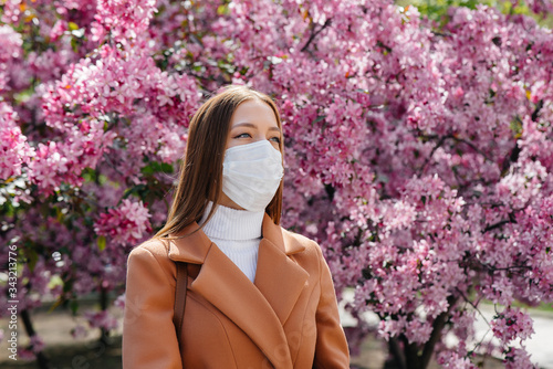 A young girl takes off her mask and breathes deeply after the end of the pandemic on a Sunny spring day, in front of blooming gardens. Protection and prevention covid 19