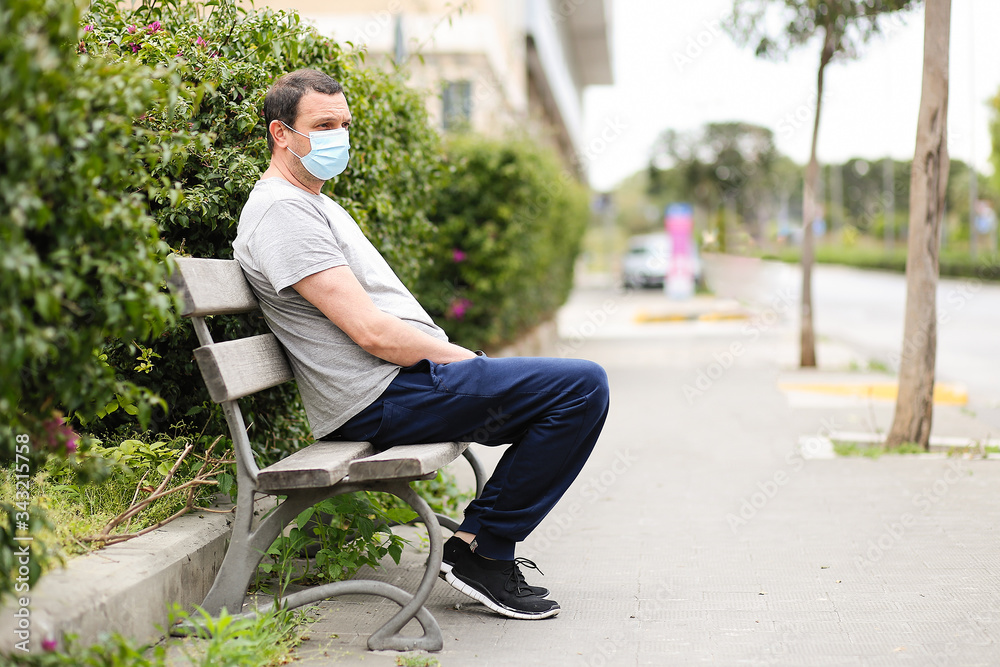 Obraz premium men in medical mask is sitting on a bench on the street during quarantine