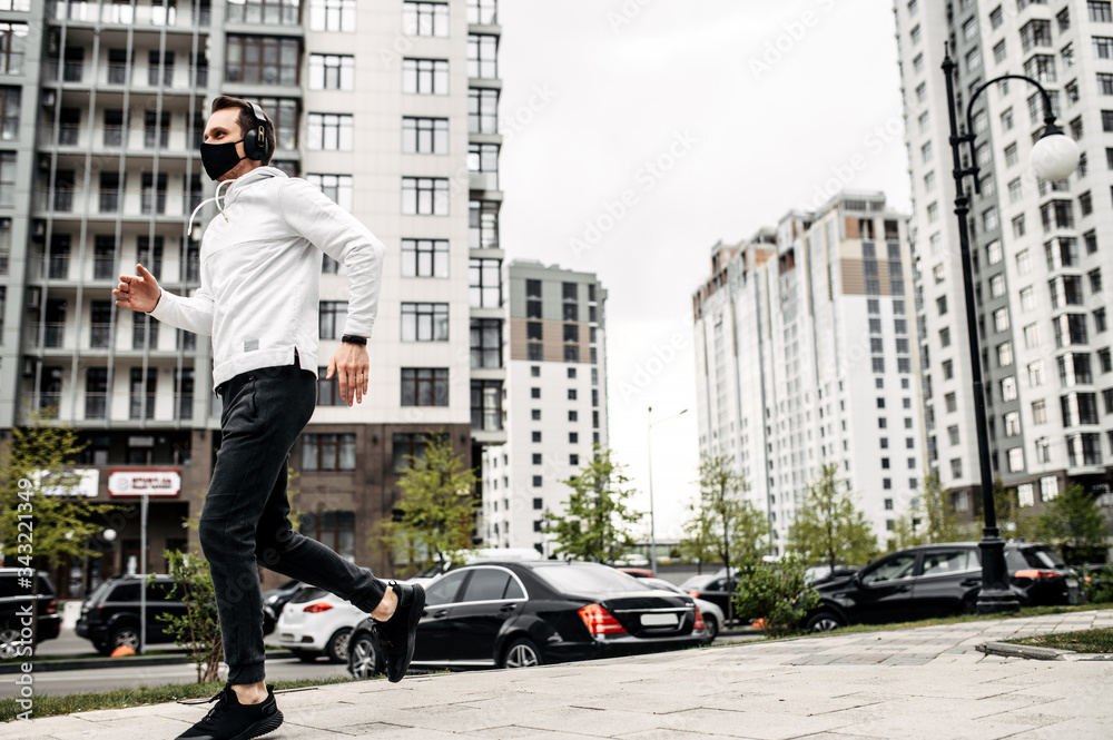 Healthy habits. Full length of young man in sports clothing in medical mask on the face is running while exercising outside
