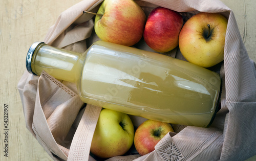 A bottle of apple juice lies in an eco bag with apples on a wooden table. photo