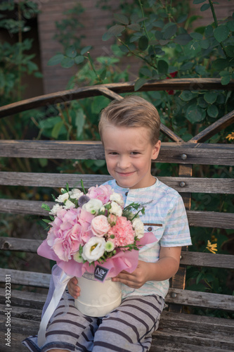 Toddler smiling boy with a large bouquet in Mothers Day for mother. Portrait of a happy little kid on a gray background. Spring background
Stylish flowers arrangement in a pink hatbox. 