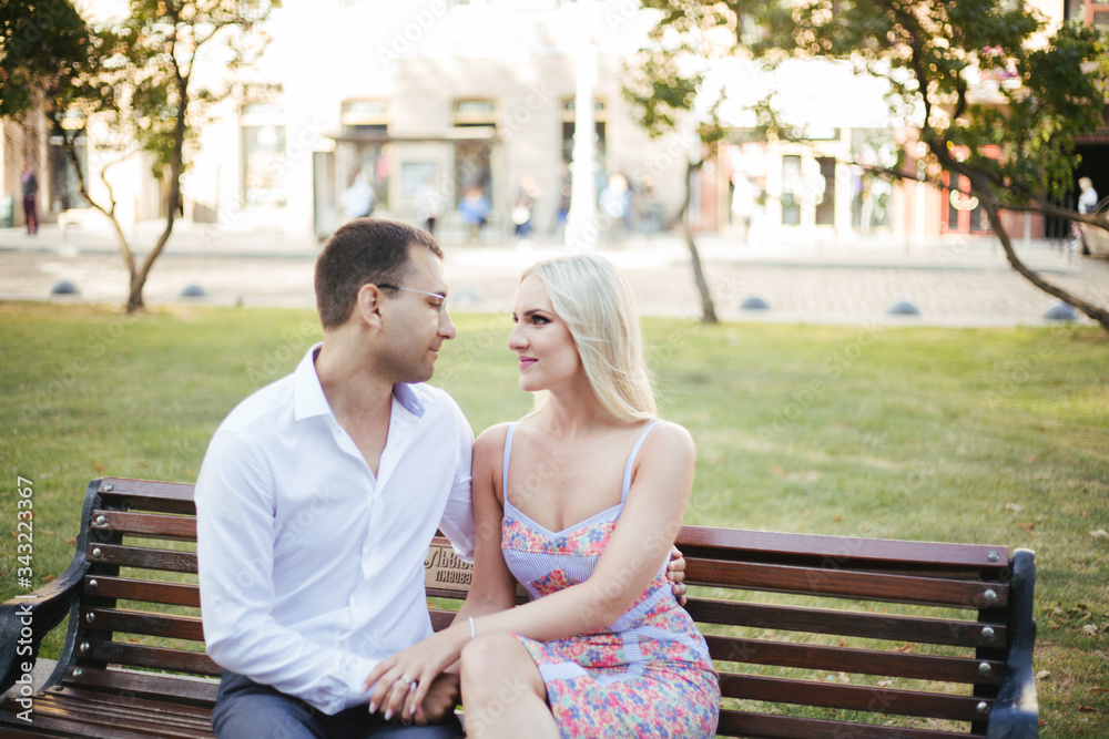 Lovely couple walking around the block. Dark-haired man in a white shirt hugging a blonde in a beautiful dress Lovely couple walking around the block. Dark-haired man in a white shirt hugging a blonde in a beautiful dress