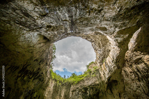 Beautiful travel destination in Bulgaria with the dramatic inside view of the eyes of God cave in Devetashka. Natural cave hole covered by nimbus dramatic rain clouds.
