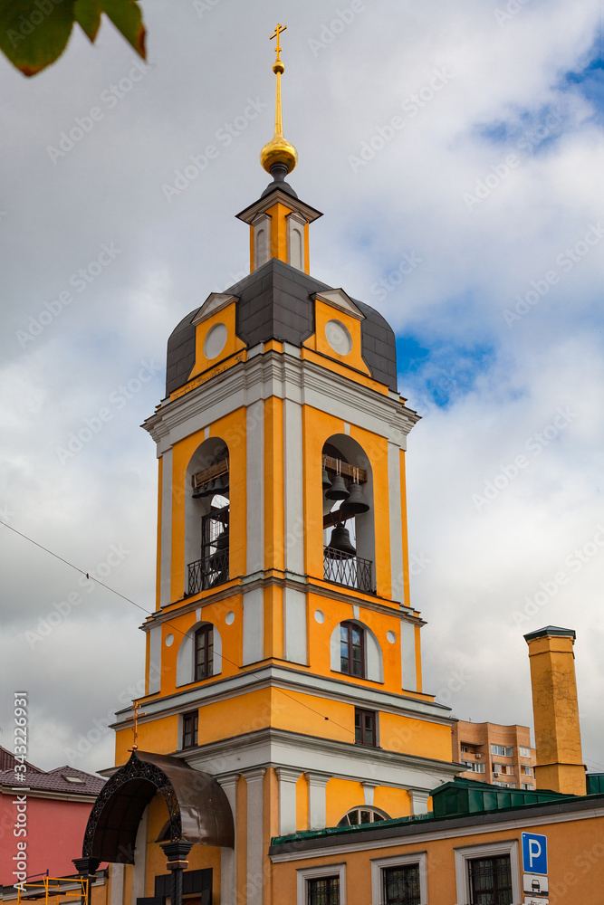 Obraz premium Tall yellow bell tower of an Orthodox church with a golden dome against a cloudy sky