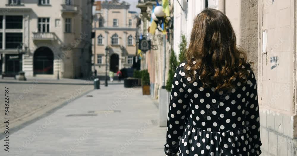 Camera follows young woman walking on the street on a beautiful sunny summer day 4K. 