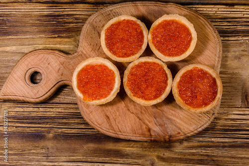 Tartlets with red caviar on a wooden cutting board. Festive food. Top view