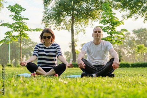 Couple, man and woman sitting in park on mat in lotus position and meditating