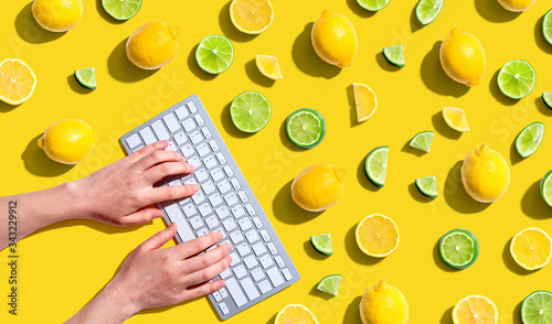 Woman using a computer keyboard with fresh lemons and limes overhead view - flat lay photo