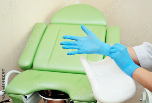 doctor gynecologist putting on rubber gloves prepares for examination against the background of a green gynecological chair.