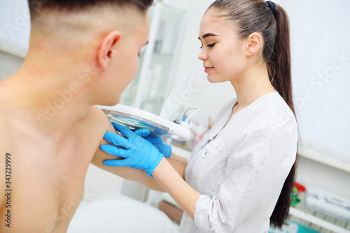 doctor dermatologist-a young woman examines the skin condition of a male patient-moles, scars, pigmentation through a special device-a cosmetic lamp magnifying glass. Prevention of melanoma