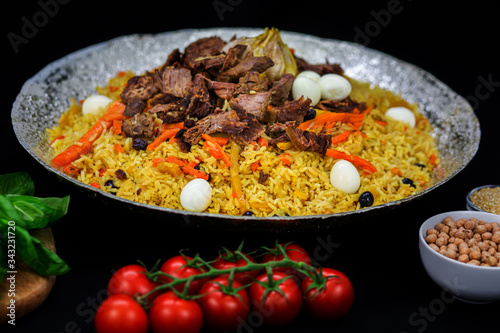 Pilaf and ingredients on plate with oriental ornament on a black background. Central-Asian cuisine - Plov Top view