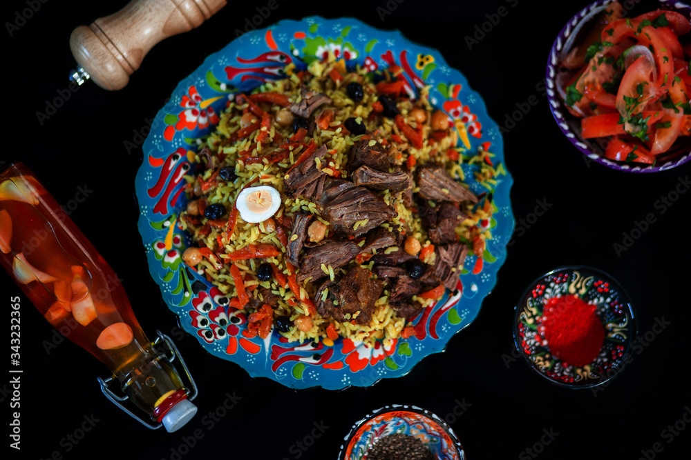 Pilaf and ingredients on plate with oriental ornament on a black background. Central-Asian cuisine - Plov Top view