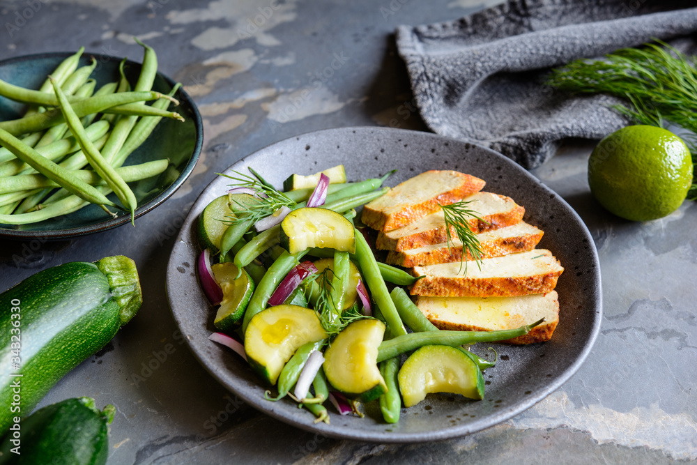 Marinated tofu slices served with blanched green beans and zucchini, drizzled with olive oil and decorated with fresh dill