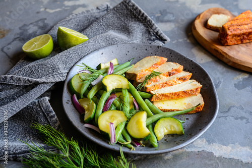 Marinated tofu slices served with blanched green beans and zucchini, drizzled with olive oil and decorated with fresh dill