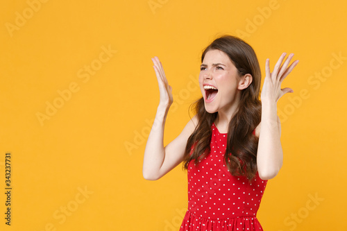 Shocked irritated young brunette woman girl in red summer dress posing isolated on yellow background studio portrait. People lifestyle concept. Mock up copy space. Spreading hands, screaming swearing.