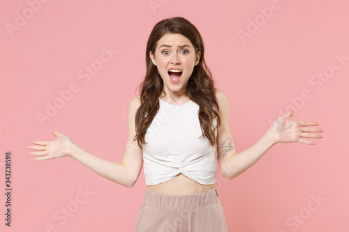Shocked perplexed young brunette woman girl in light casual clothes posing isolated on pastel pink background studio portrait. People emotions lifestyle concept. Mock up copy space. Spreading hands. © ViDi Studio