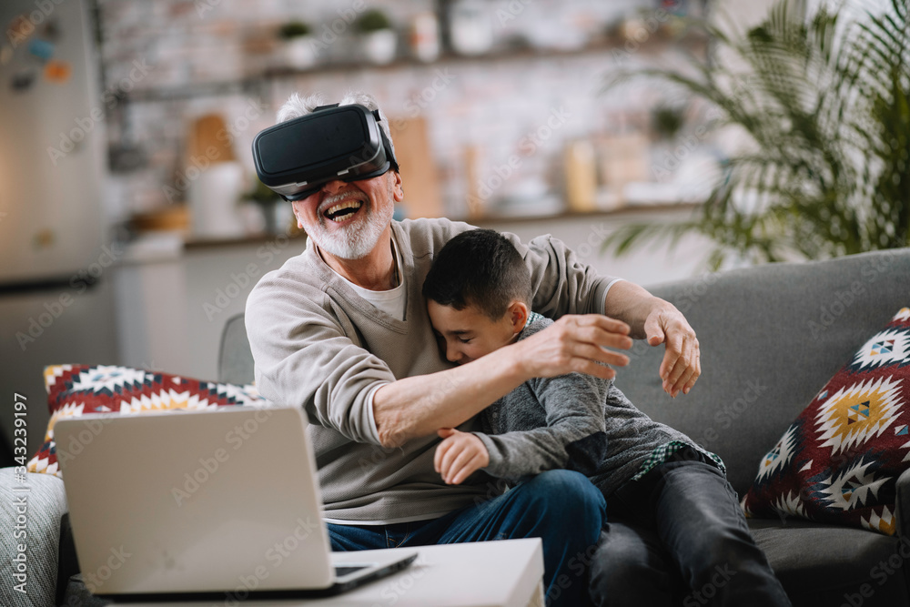 Grandson and his grandpa playing with VR at home on sofa. Grandfather and a little boy having fun at home. Grandson and his grandpa playing with VR at home on sofa. Grandfather and a little boy having fun at home.