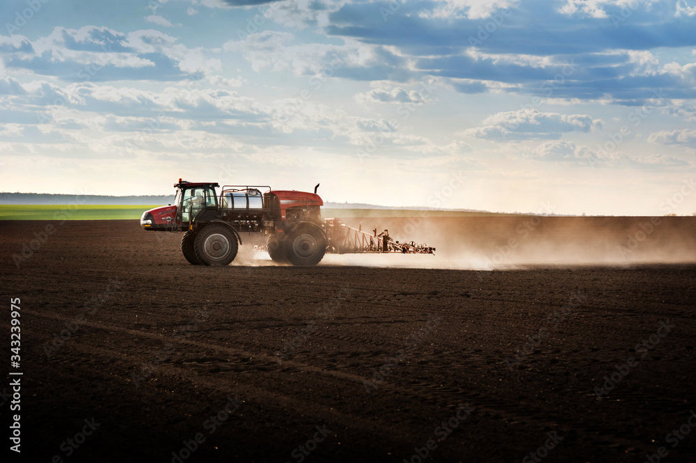 Fototapeta premium Big self-propelled red sprayer in the field cultivates arable land against the light