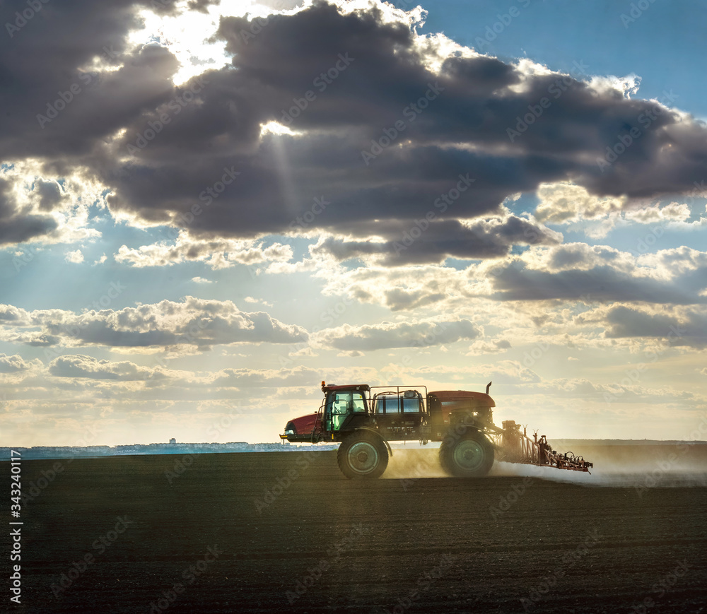 Fototapeta premium a self-propelled sprayer in the field cultivates arable land against the fantastic light from under the clouds