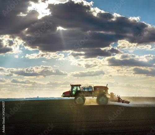 a self-propelled sprayer in the field cultivates arable land against the fantastic light from under the clouds