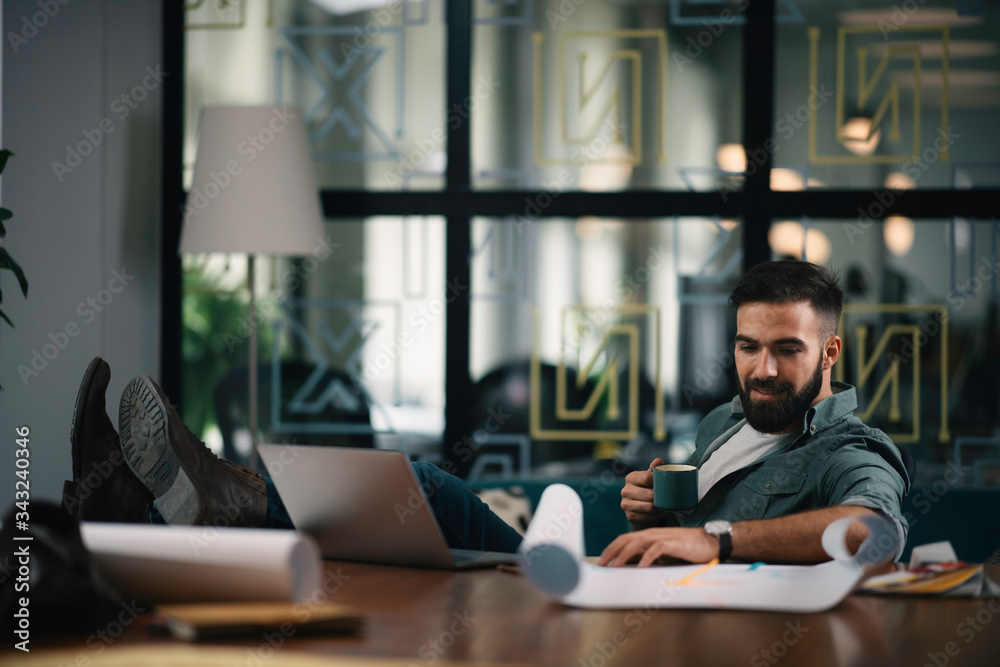 Handsome man drinking coffee in office. Young man working on project.