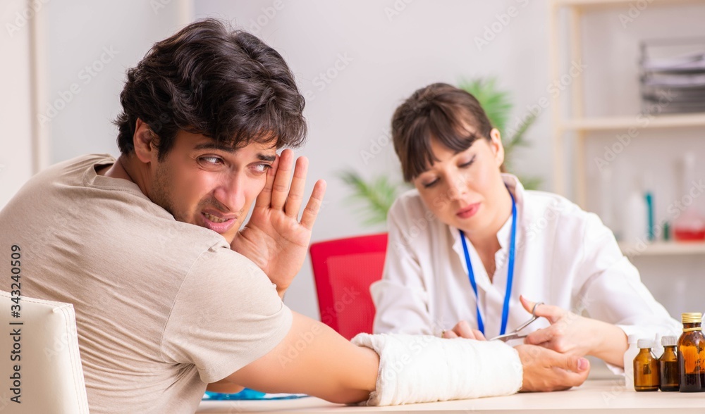 Young man with bandaged arm visiting female doctor traumatologis Young man with bandaged arm visiting female doctor traumatologis