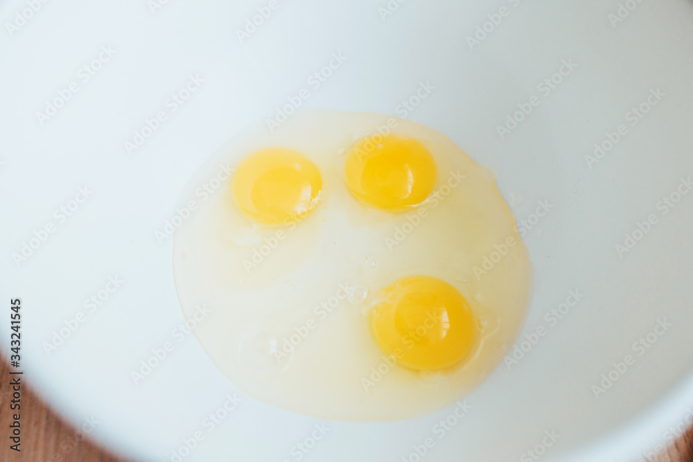 Three chicken eggs with a bright yolk in a white plastic bowl - kitchen utensil Three chicken eggs with a bright yolk in a white plastic bowl - kitchen utensil