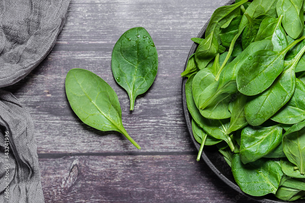 Fototapeta premium Fresh organic baby spinach leaves on a plate on dark wooden table top view. Healthy and organic food concept.