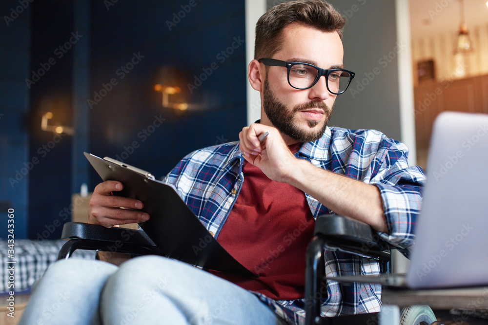 Disabled young man making notes in notepad while using laptop Stock ...
