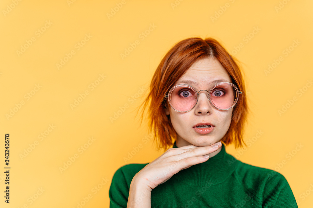 Charming young woman in glasses stands on a background of yellow wall