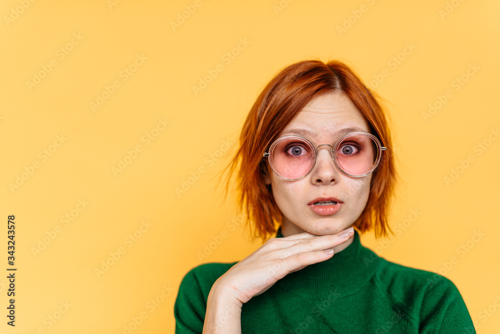 Charming young woman in glasses stands on a background of yellow wall Charming young woman in glasses stands on a background of yellow wall