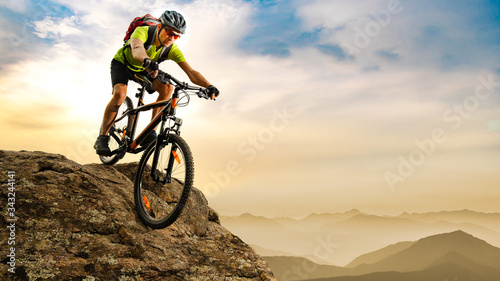 Cyclist Riding the Bike Down the Rock at Sunrise in the Mountains. Extreme Sport and Enduro Biking Concept. photo