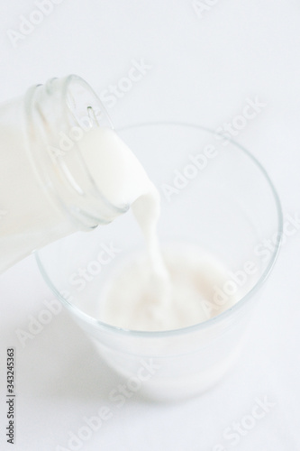 Minimal set of a glass bottle pouring white liquid milk in a glass, with white background