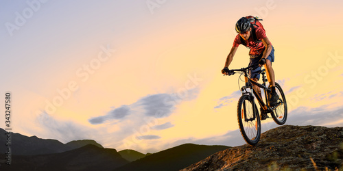 Cyclist in Red Riding the Bike Down the Rock at Sunset. Extreme Sport and Enduro Biking Concept.