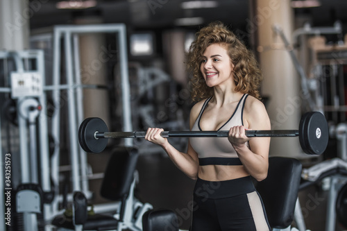 Slim woman, blonde girl in sportwear with dumbbells in a gym, exercising with a barbell