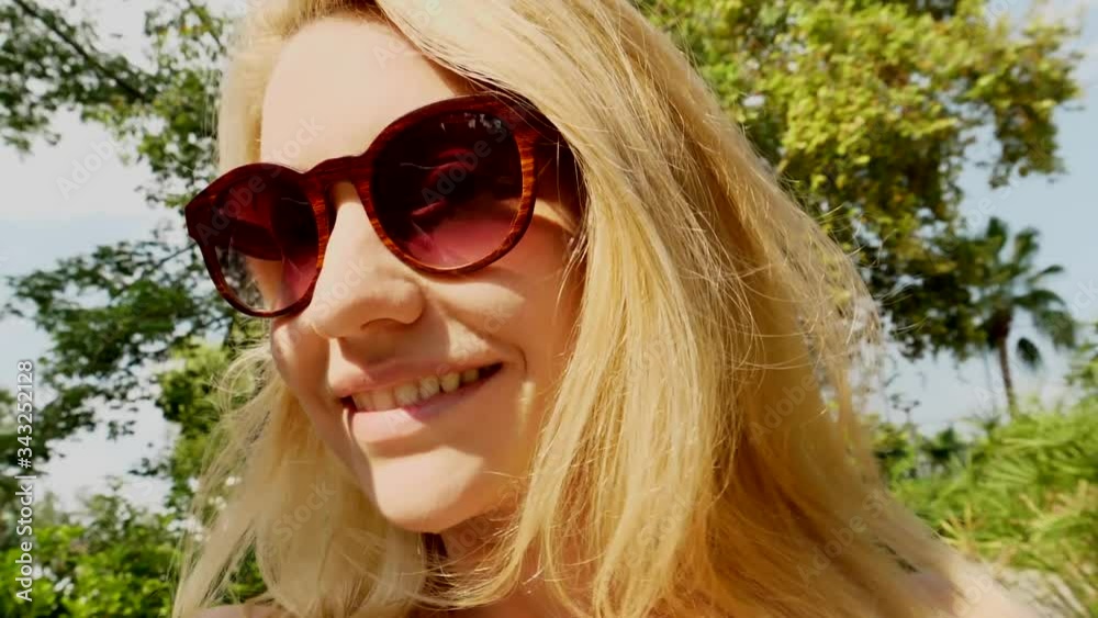 Cute blonde girl smiles and examines the rainforest through sunglasses.