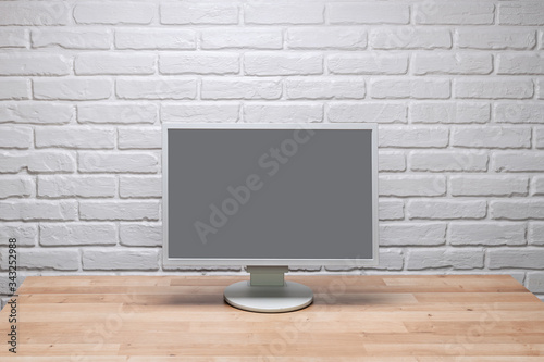 Blank screen computer monitor on working desk with brick wall