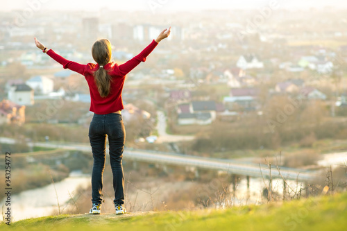 Young woman standing outdoors raising her hands enjoying city view. Relaxing, freedom and wellness concept.